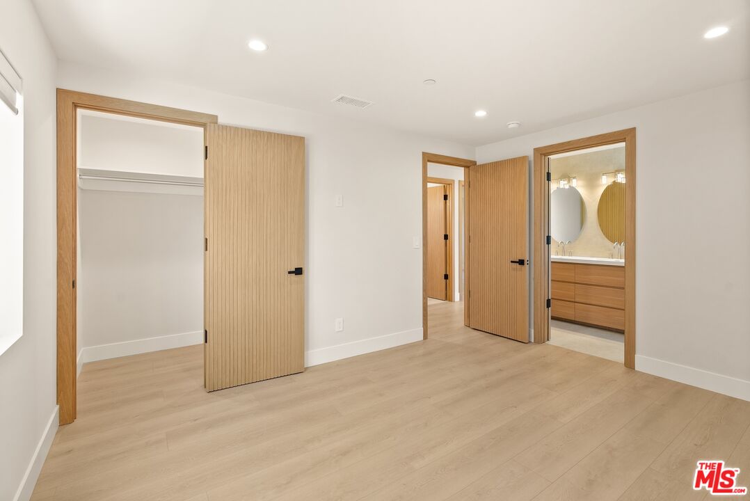 Unfurnished room with light wood floors, an open closet, and a bathroom vanity visible through the doorway.