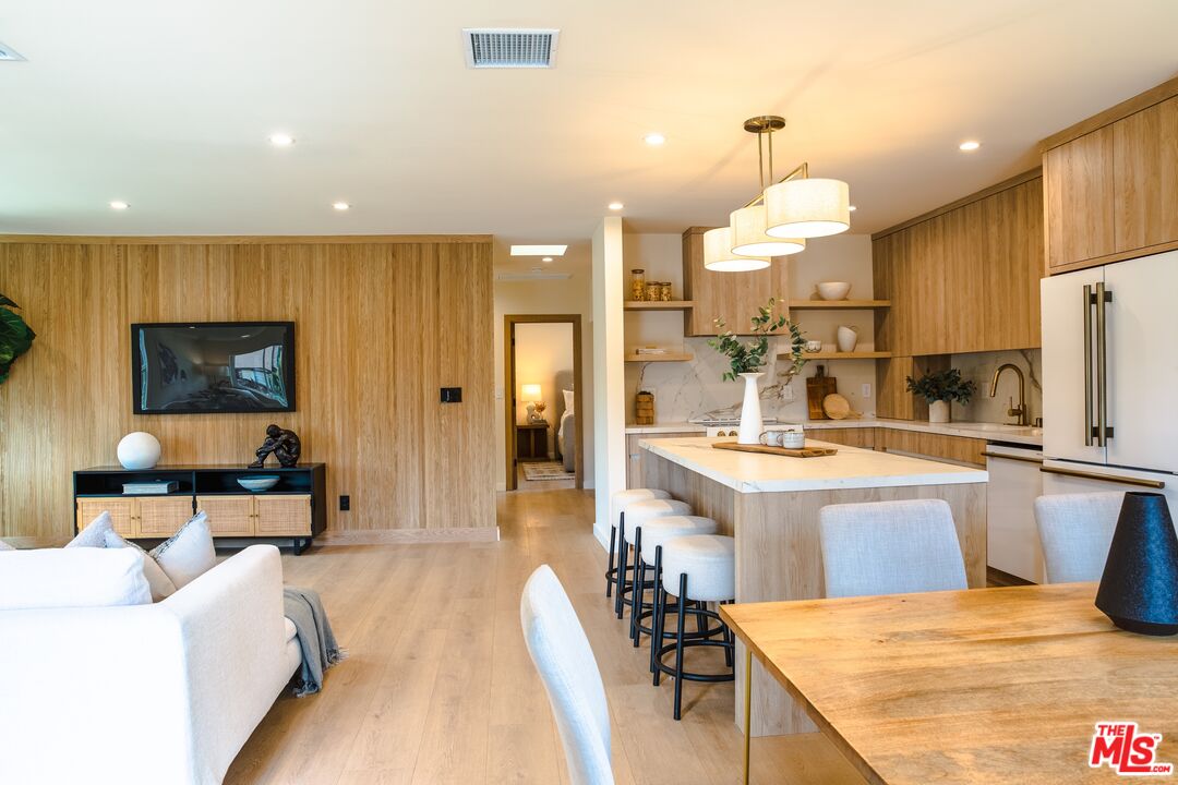 Open-plan kitchen and living room with a wood-paneled island, bar stools, and light wood floors.