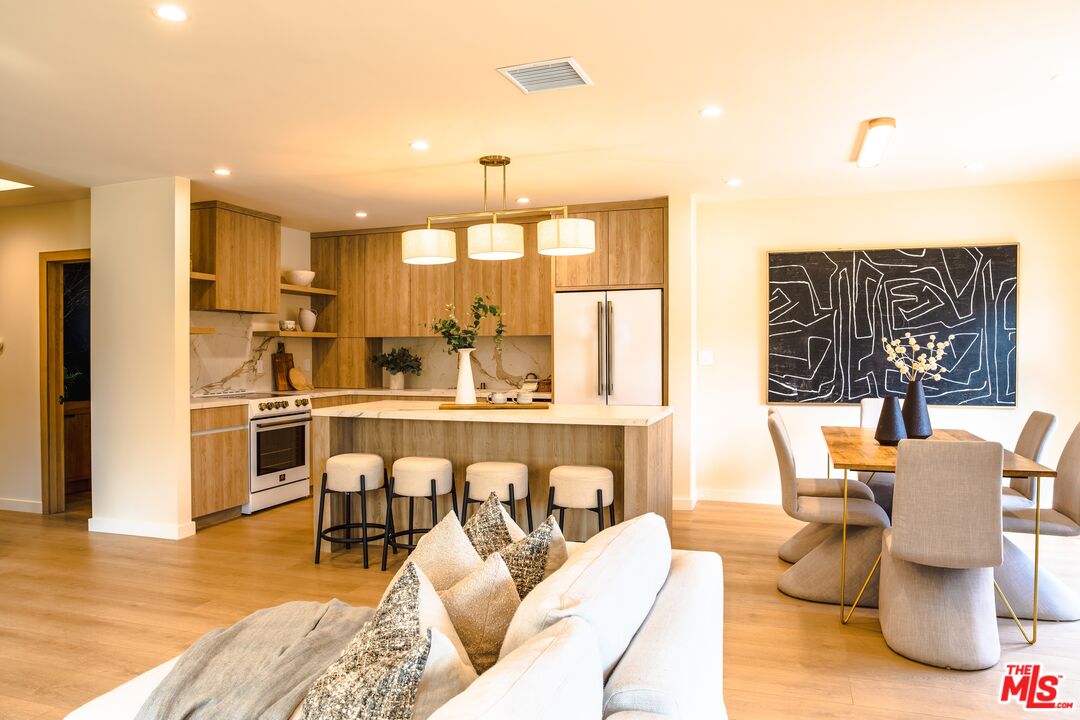 Open-plan kitchen and living room with a wood-cabinet island, white sofa, and dining area.