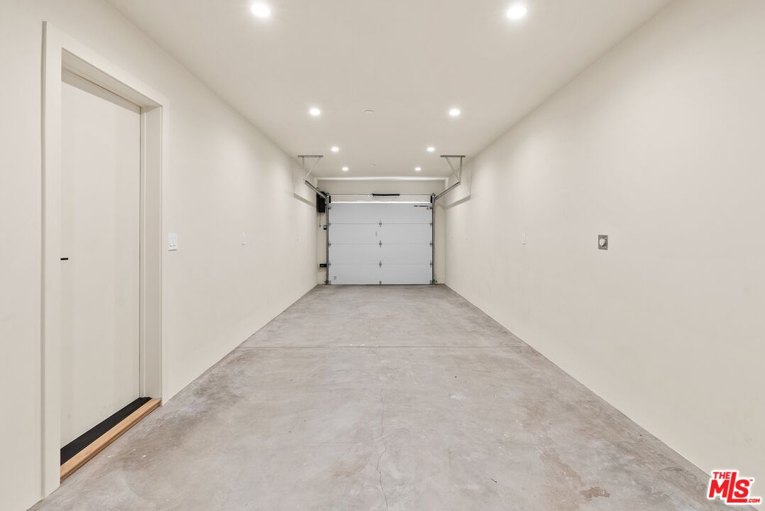 Empty garage with a gray concrete floor, recessed lights, and a white overhead door.