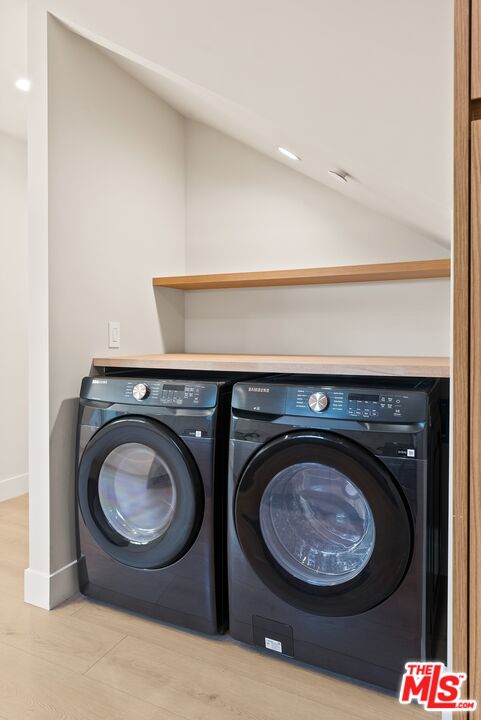 Side-by-side dark front-loading washer and dryer beneath a sloped ceiling and wood shelf.