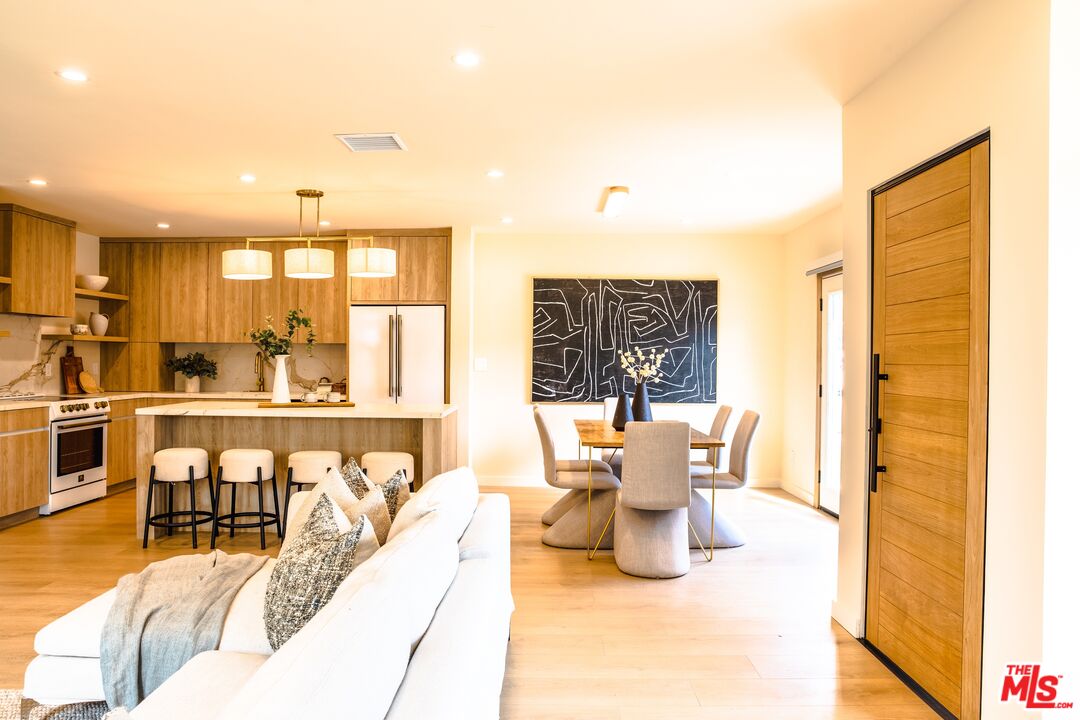 Open-plan living room, dining area, and kitchen with warm wood cabinetry and a white sofa.