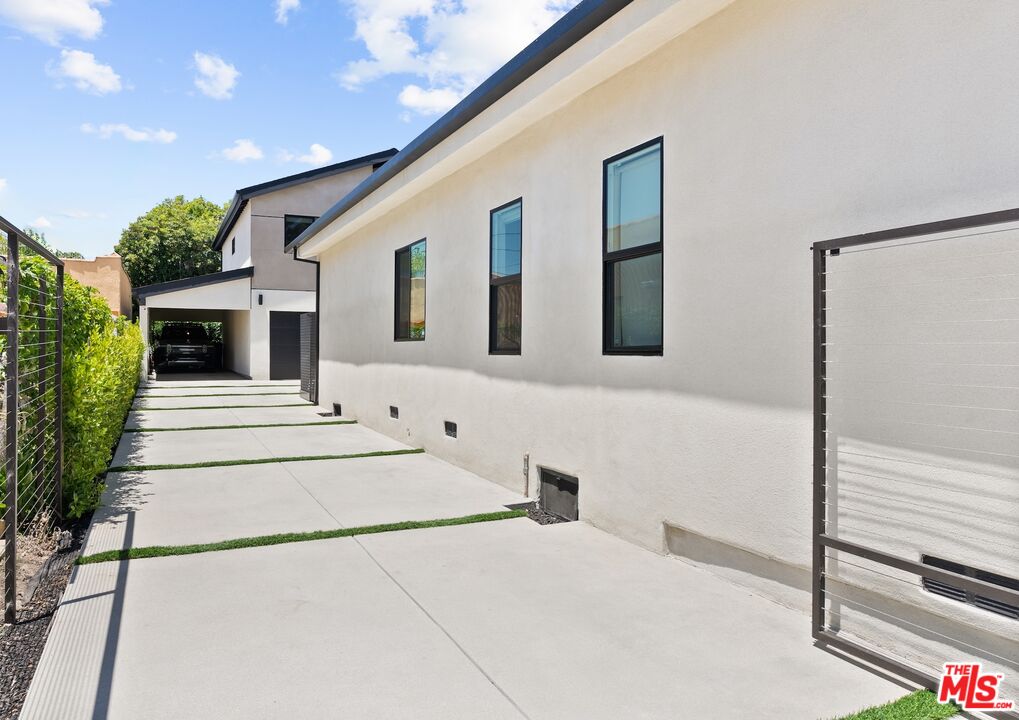 Modern stucco home beside a long concrete driveway leading to a covered garage.