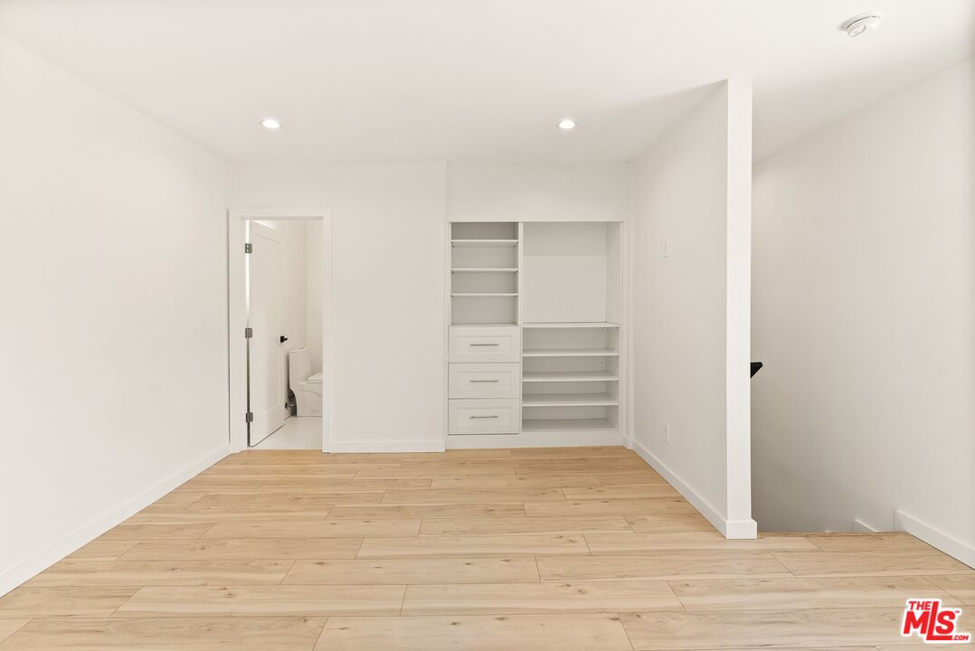 Vacant room with built-in white shelving, drawers, and light wood plank flooring.