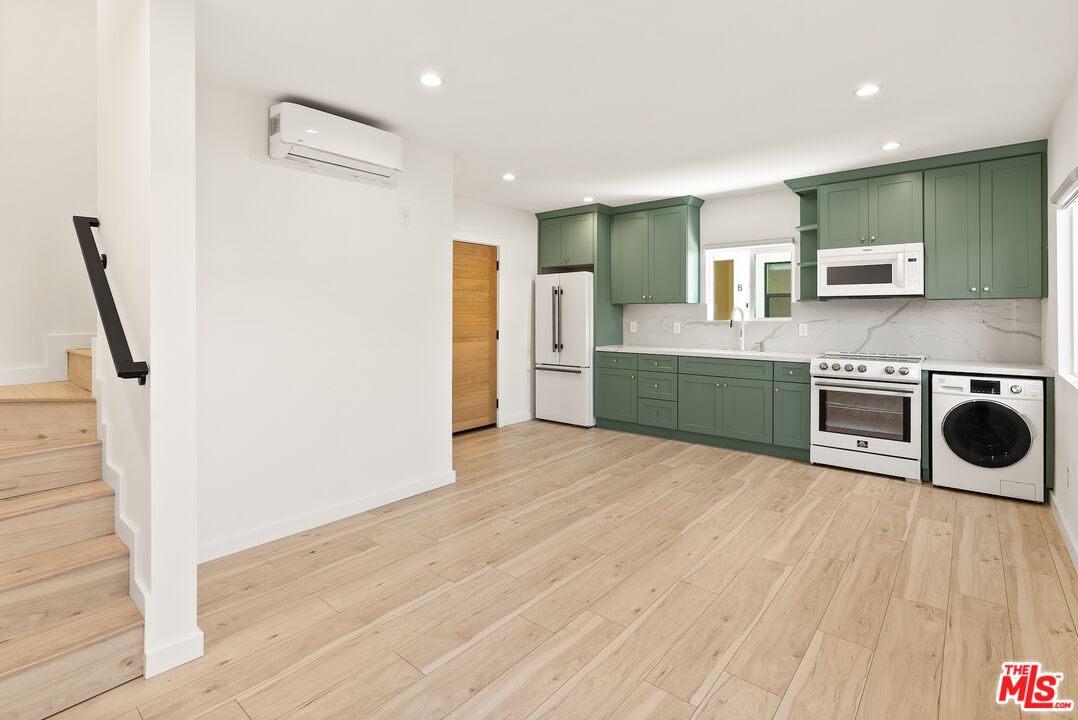 Unfurnished kitchen with sage-green cabinets, light wood floors, and a washer beside the stove.