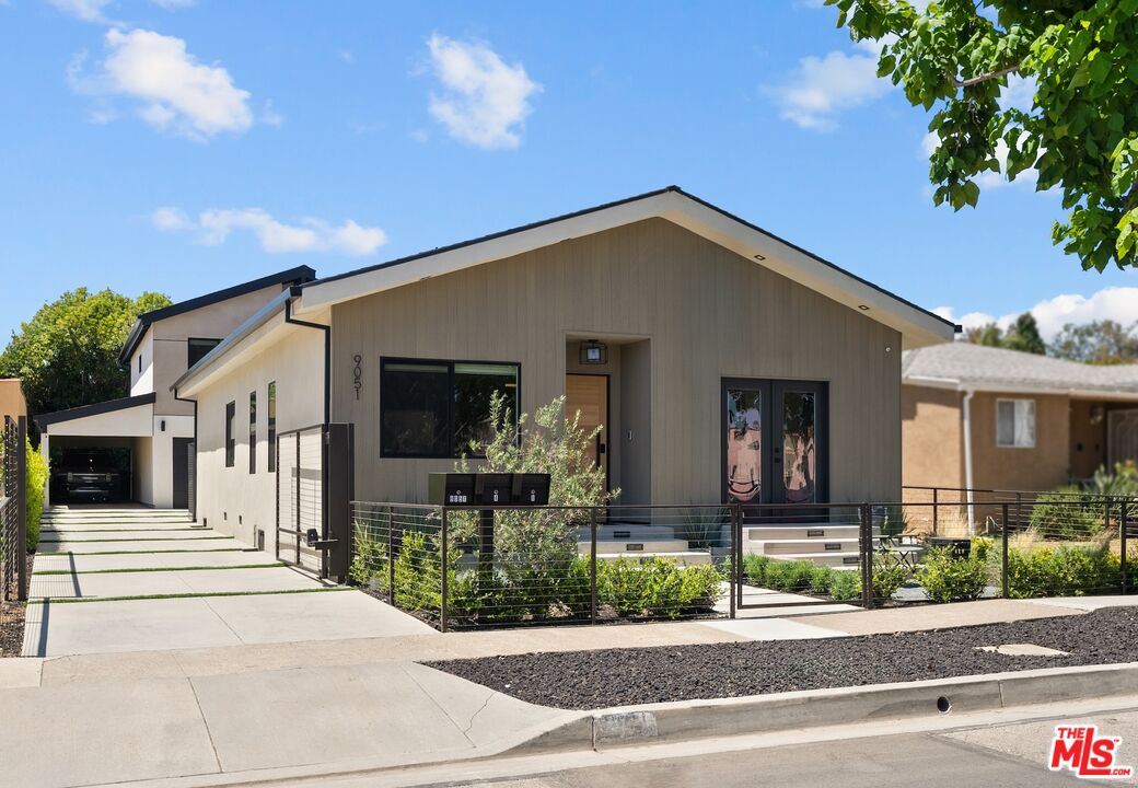 Contemporary single-story home with a front gable, metal fence, and broad concrete driveway.
