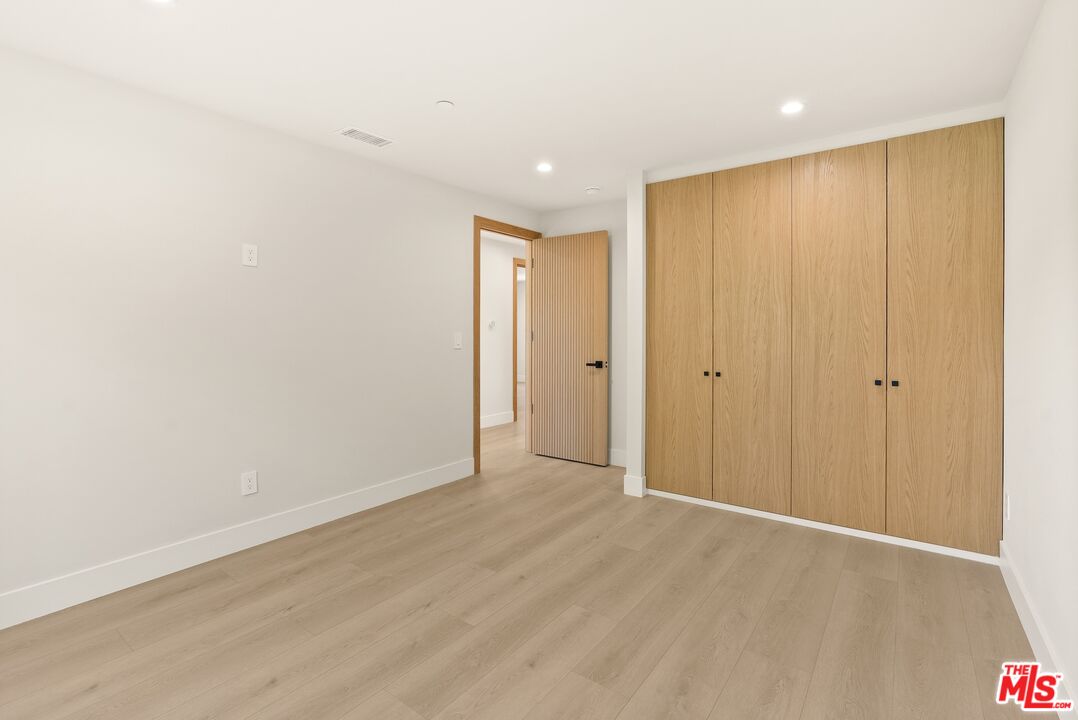Empty room with light wood floors and tall wood closet doors.