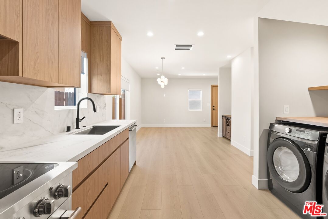 Kitchen with wood cabinetry and stone counters, opening to a laundry area with washer and dryer.