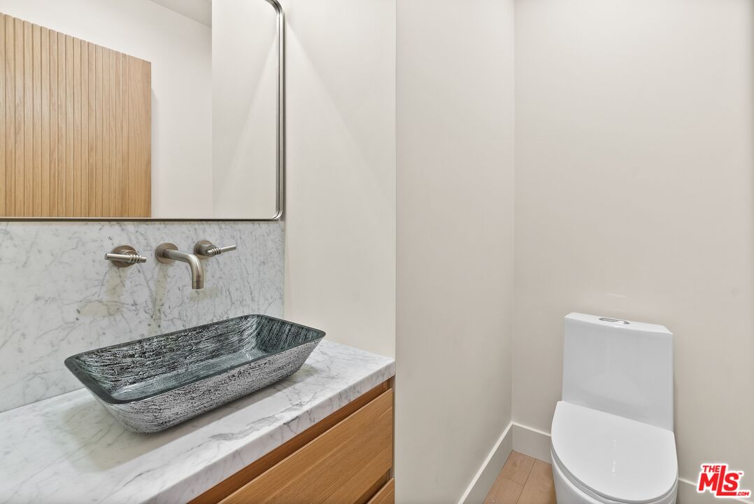 Modern bathroom vanity with a dark vessel sink, marble surfaces, wood cabinetry, and adjacent toilet.