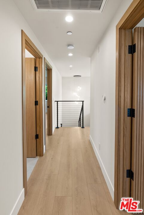 Bright hallway with light wood flooring, wood-trimmed doorways, and a black railing