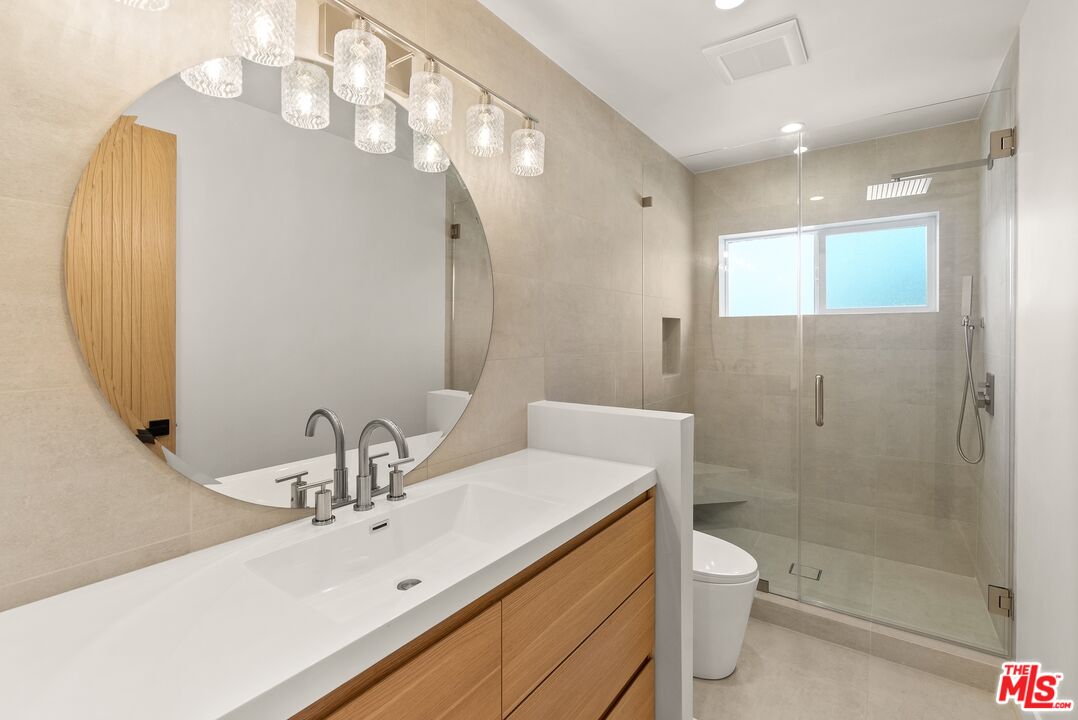 Bathroom with a long wood vanity, oversized round mirror, and glass shower beside a window.