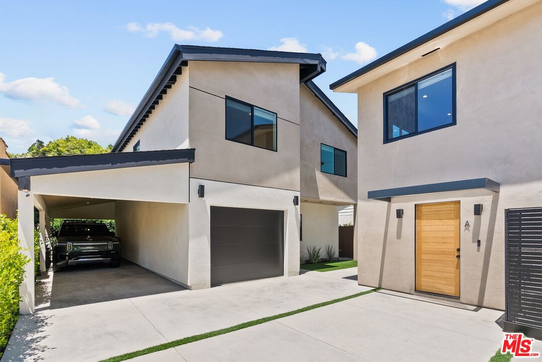 Modern stucco residence with a wooden entry door, two garages, and a covered carport.