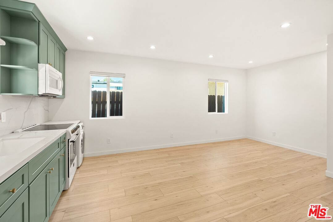 Empty kitchen with sage-green cabinetry, white counters, and light wood floors.