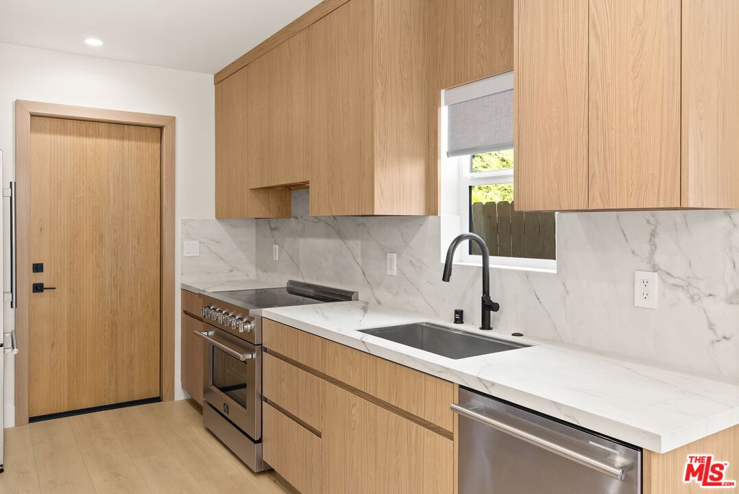 Modern kitchen with light wood cabinets, veined stone backsplash, and stainless steel appliances.