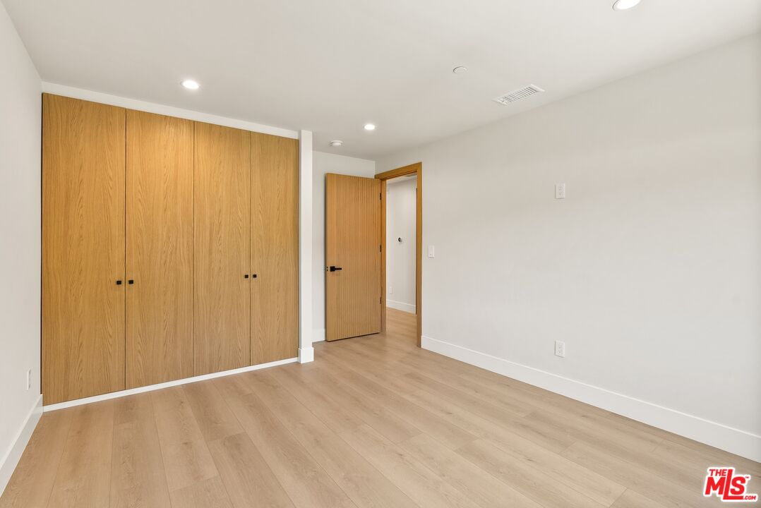 Empty room with wide wood closet doors, light wood flooring, and an open doorway.