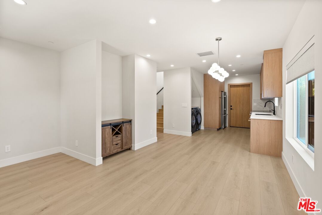 Open-plan living area with pale wood floors, light wood kitchen cabinetry, and large windows.