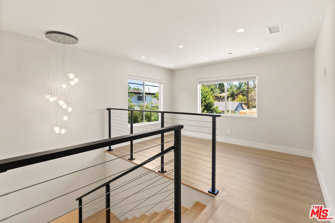 Upstairs landing with black cable railing, light wood floors, and a modern chandelier.