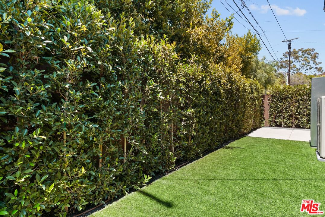 Side yard with artificial turf and a tall hedge along the property line.