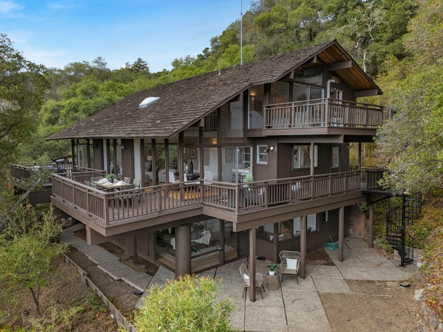 Multi-level wood home with wraparound decks and a patio, surrounded by trees.