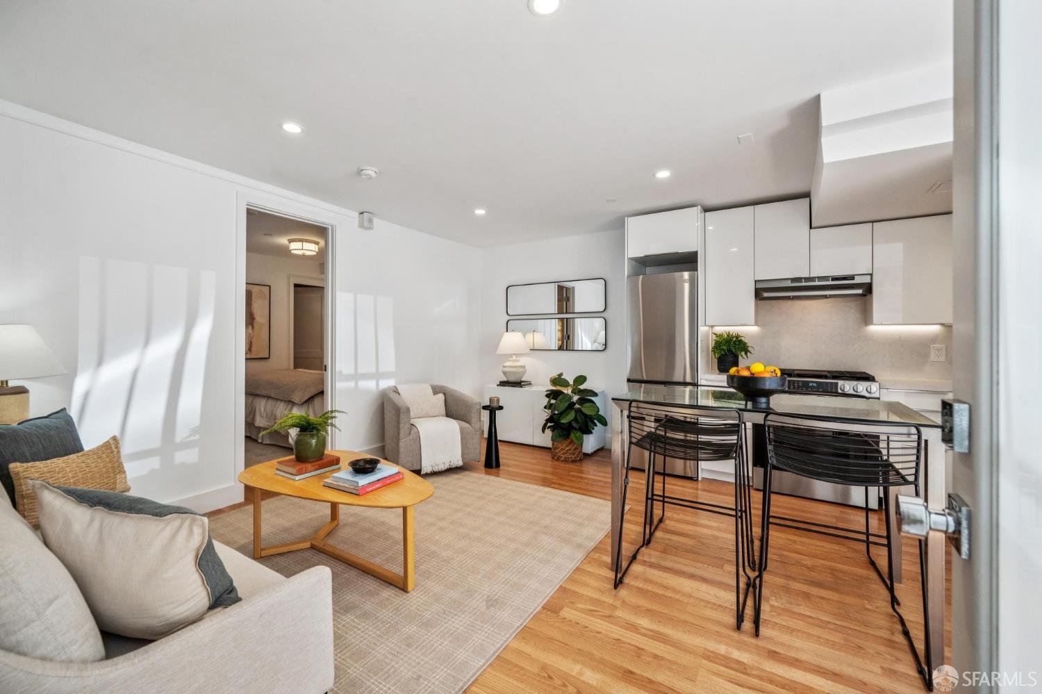 Open-plan living room and kitchen with white cabinetry, stainless steel appliances, and hardwood floors.