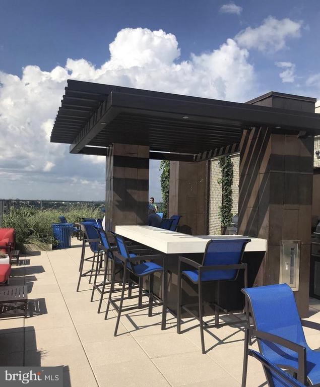 Rooftop terrace with blue dining chairs and a long table beneath a modern pergola.