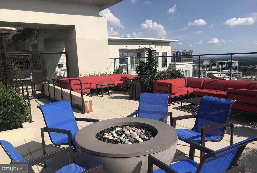 Rooftop terrace with a circular fire pit, blue chairs, red sofas, and city views.