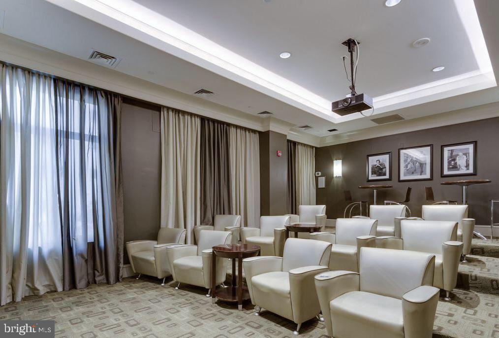 Furnished meeting room with white armchairs, small tables, and a ceiling-mounted projector.