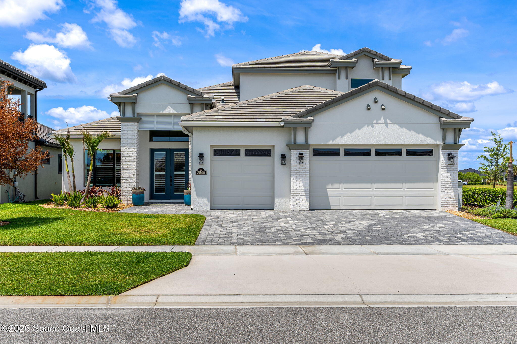 Light-colored home with a tiled roof, stone accents, and a wide paver driveway.
