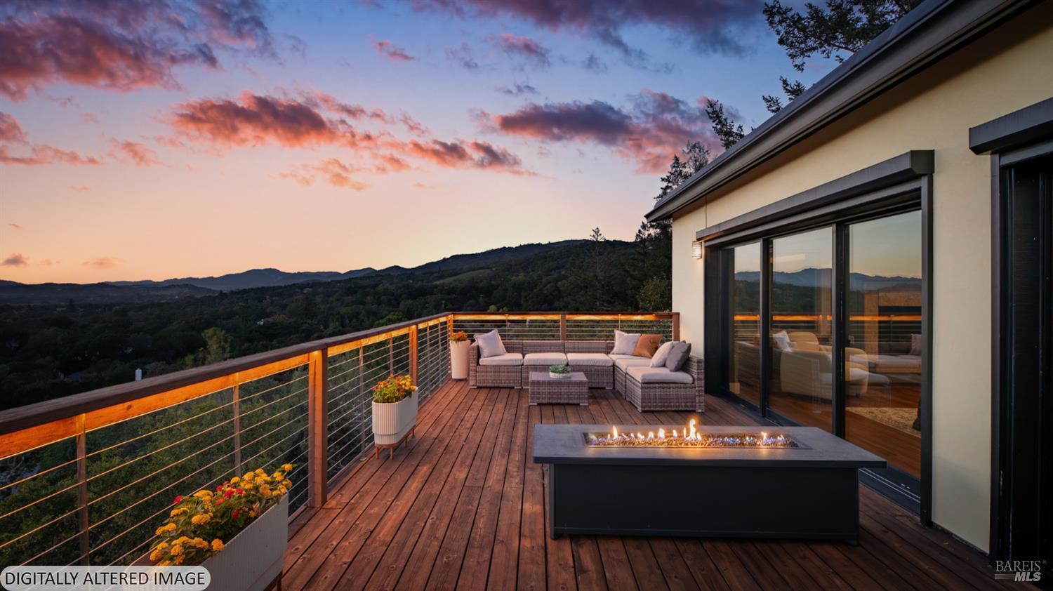 Wooden deck with lounge seating and a fire table overlooking wooded hills at sunset.