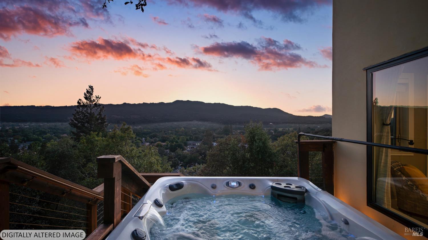 Outdoor hot tub on a deck overlooking a wooded valley and mountain ridge at sunset.