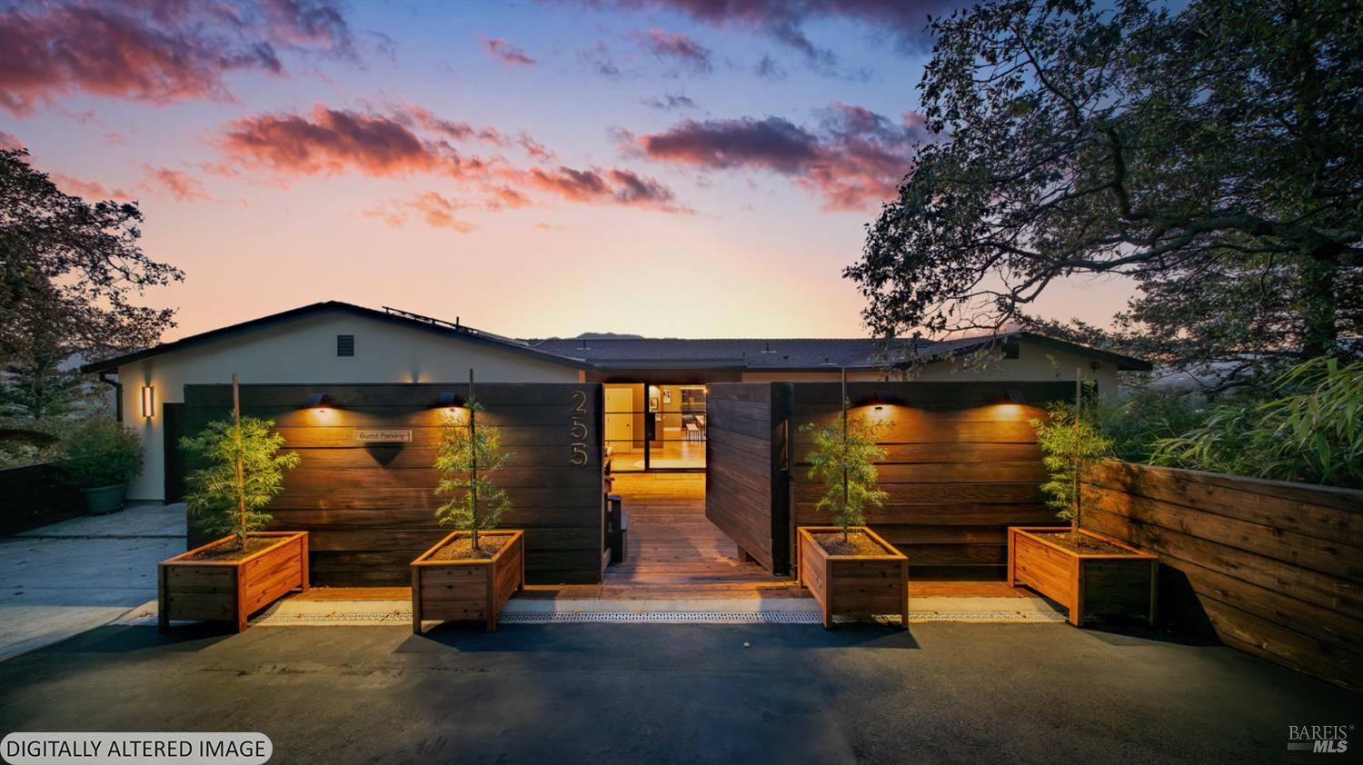 Modern single-story home at dusk, with an illuminated entrance behind a wood fence and planters.