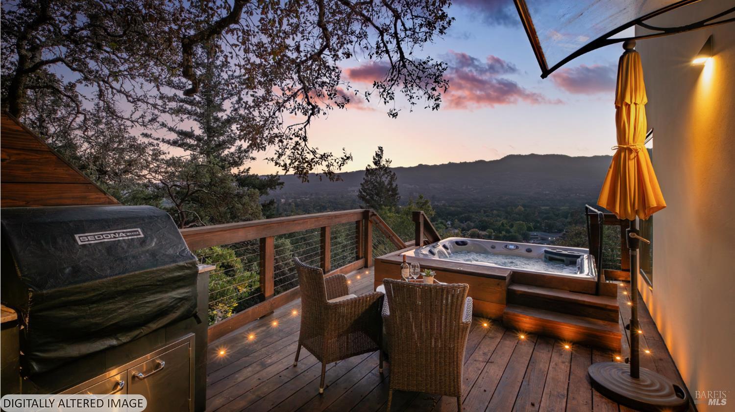 Furnished deck with a hot tub overlooking a wooded valley at dusk.
