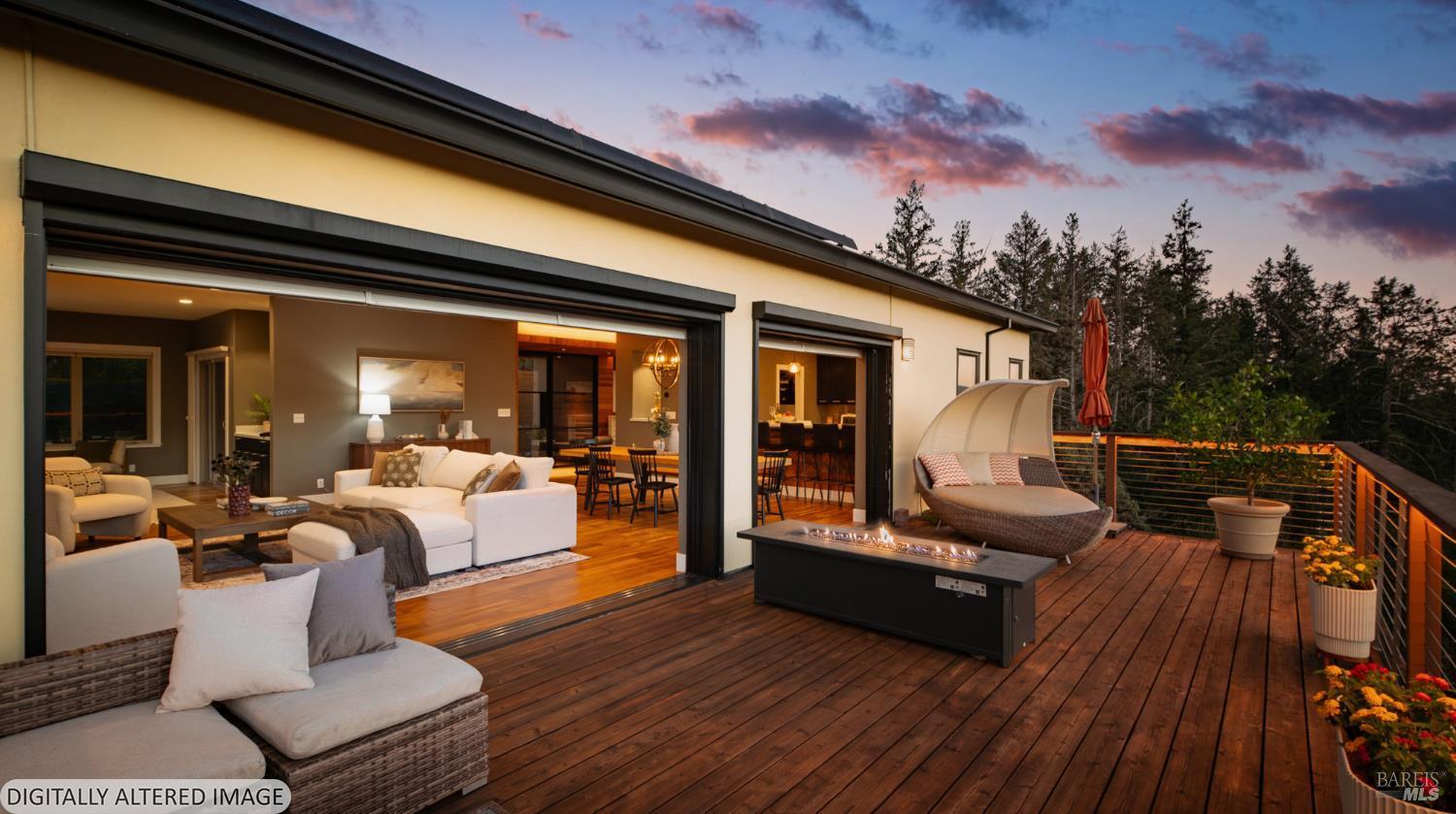 Modern home with open sliding doors onto a furnished wood deck and outdoor fire table at dusk.