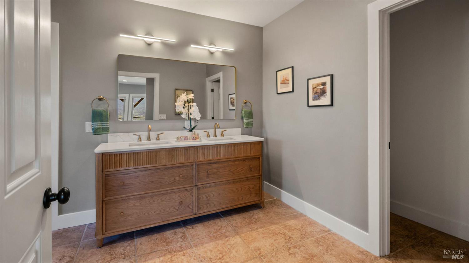Bathroom with a walnut double vanity, wide mirror, and terracotta-colored tile floor.