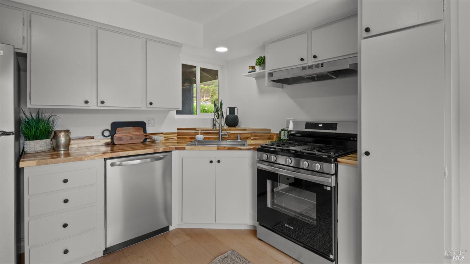 Kitchen with white cabinets, butcher-block counters, stainless dishwasher, and black gas range.