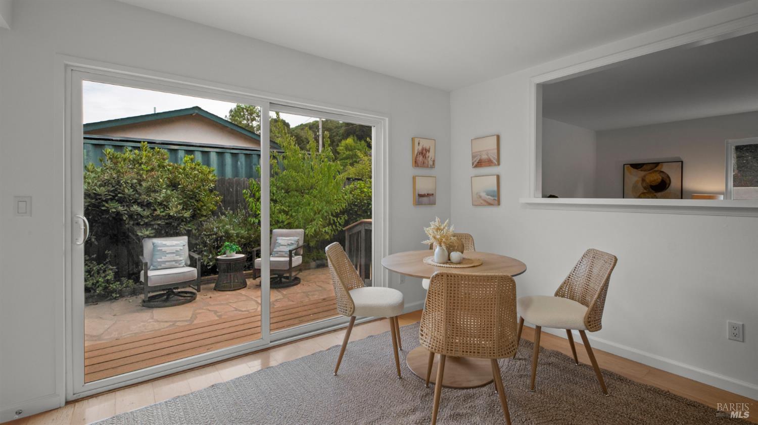 Dining room with a round table and woven chairs beside sliding glass doors to a leafy patio.
