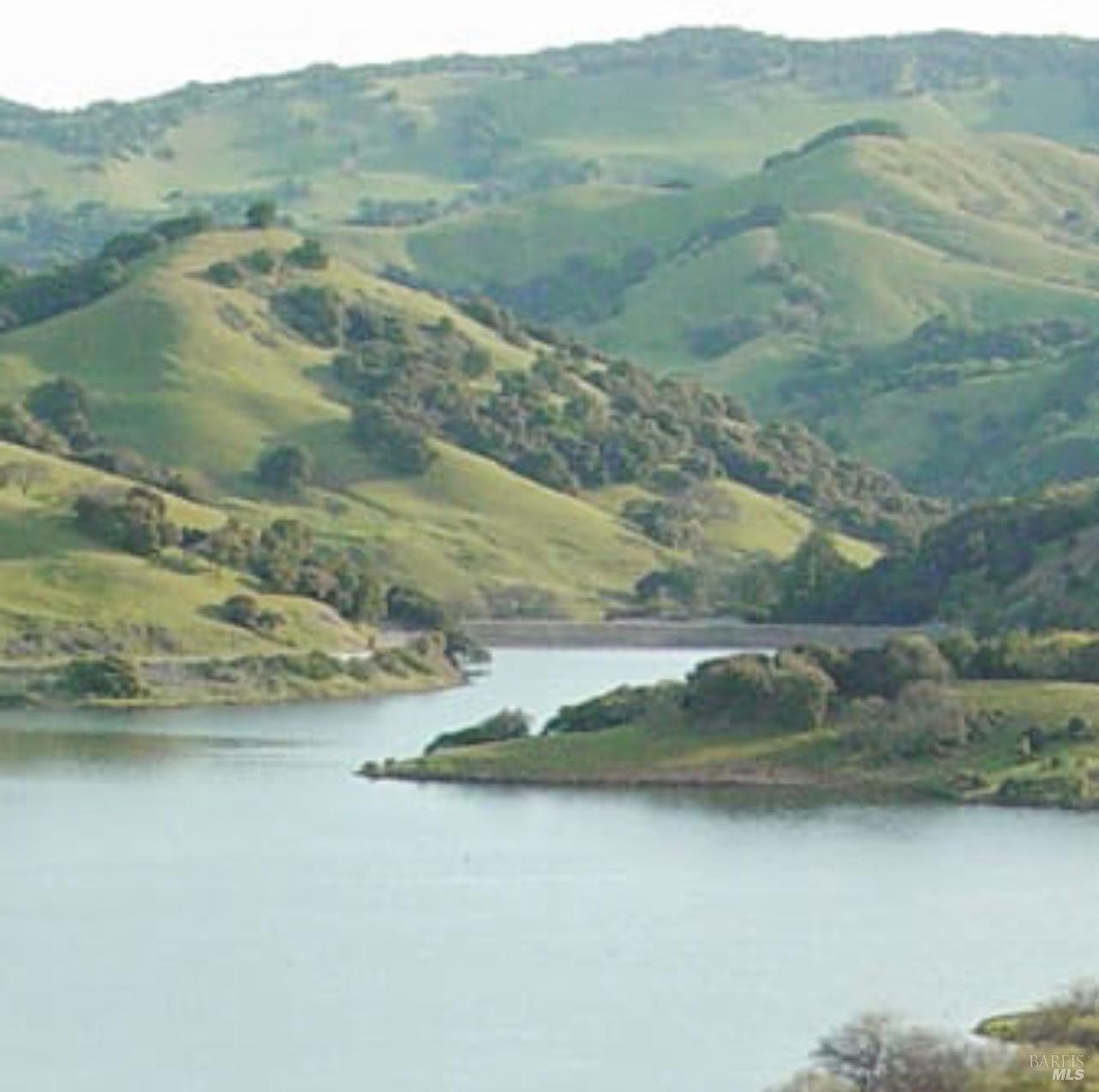 Body of water bordered by rolling green hills and a wooded shoreline.