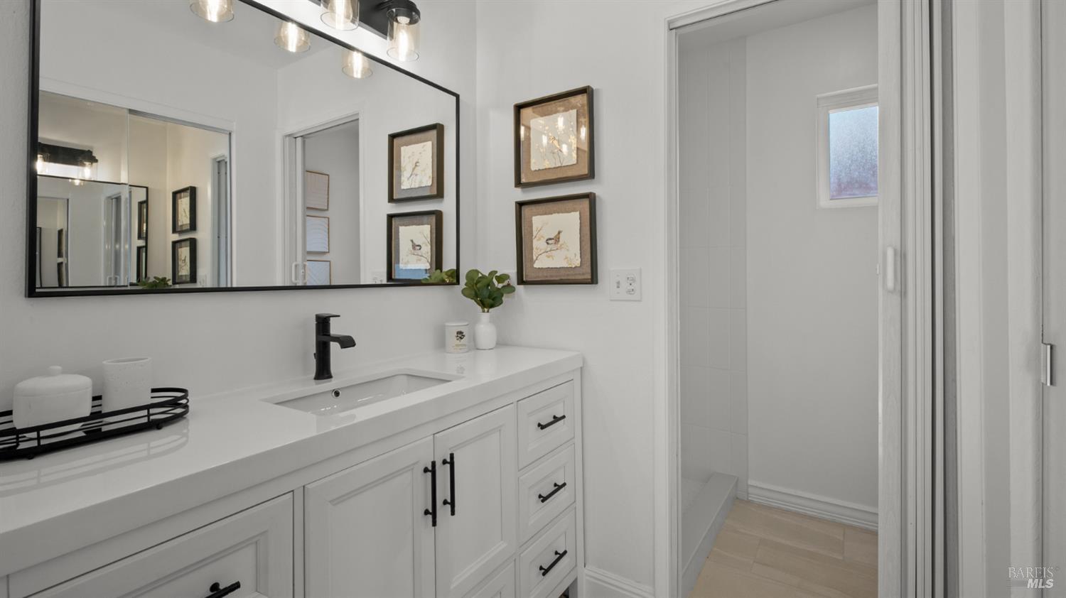 Bathroom with a white vanity and black fixtures beside a tiled shower.