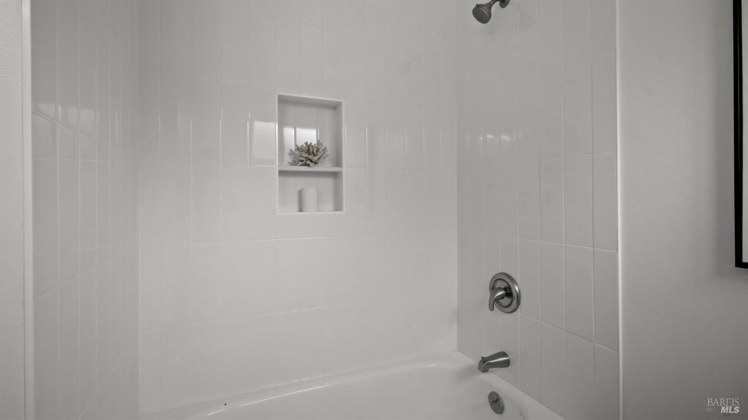 White tiled bathtub and shower alcove with a recessed shelf and chrome fixtures.