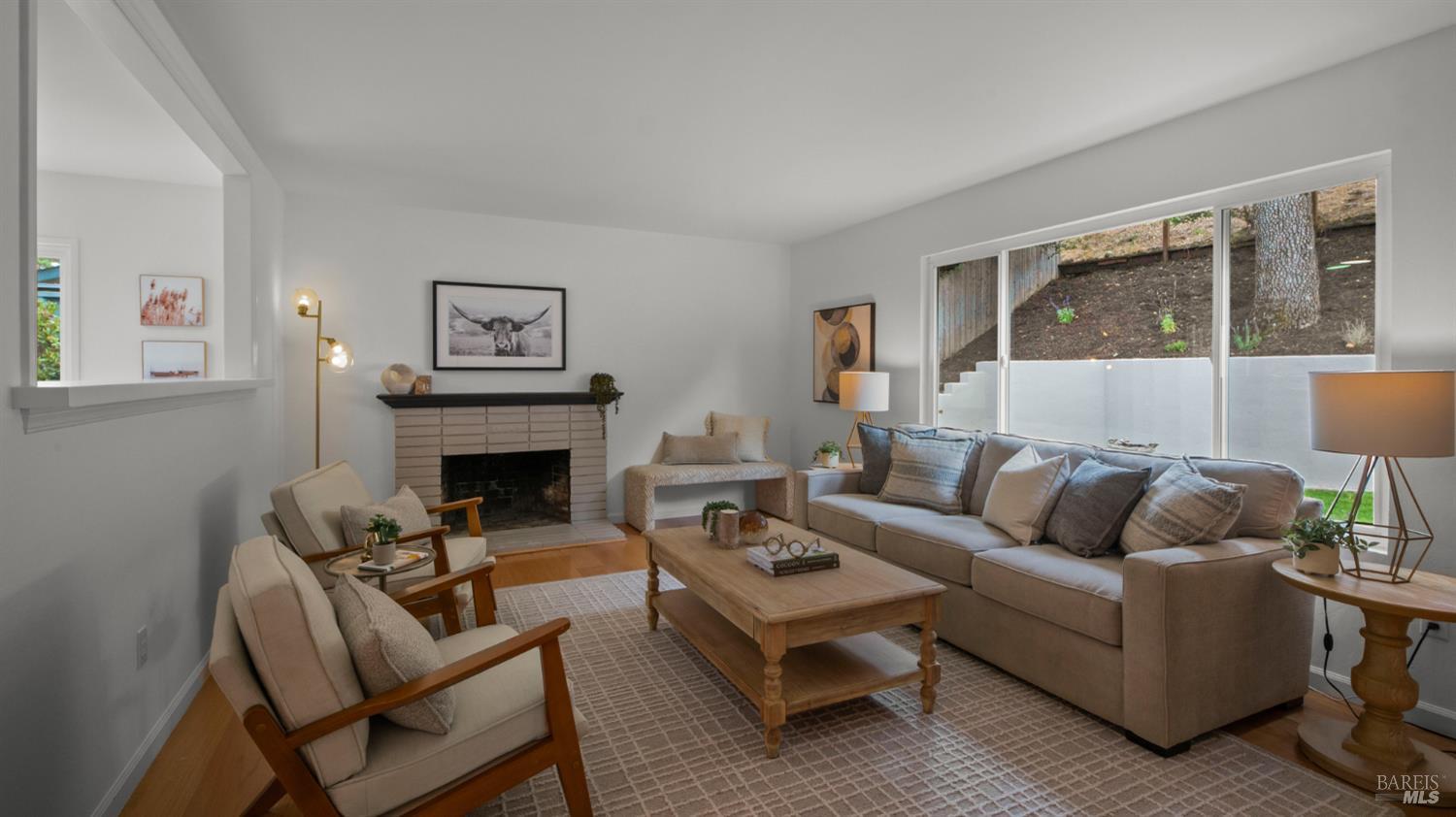 Staged living room with a brick fireplace, neutral seating, and sliding glass doors overlooking a wooded slope.