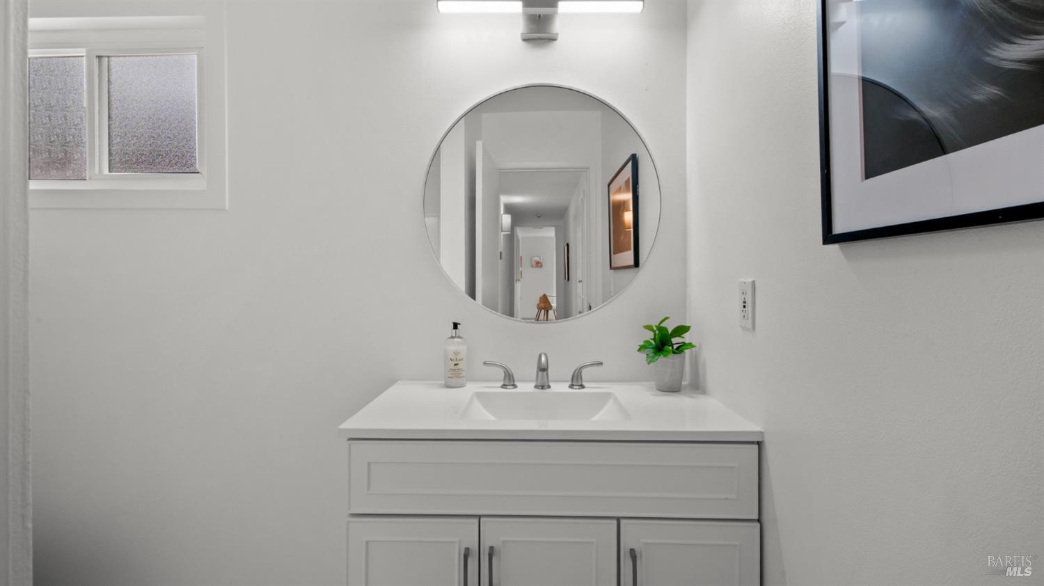 Bathroom vanity with a round mirror, white cabinetry, and chrome faucet.