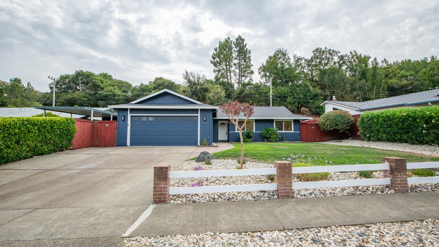 Blue single-story home with a wide garage, concrete driveway, and low white fence.