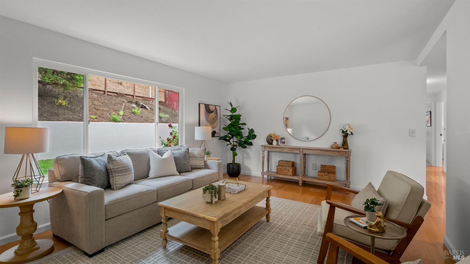 Living room with a gray sectional, wood coffee table, patterned rug, and large windows overlooking a landscaped slope.