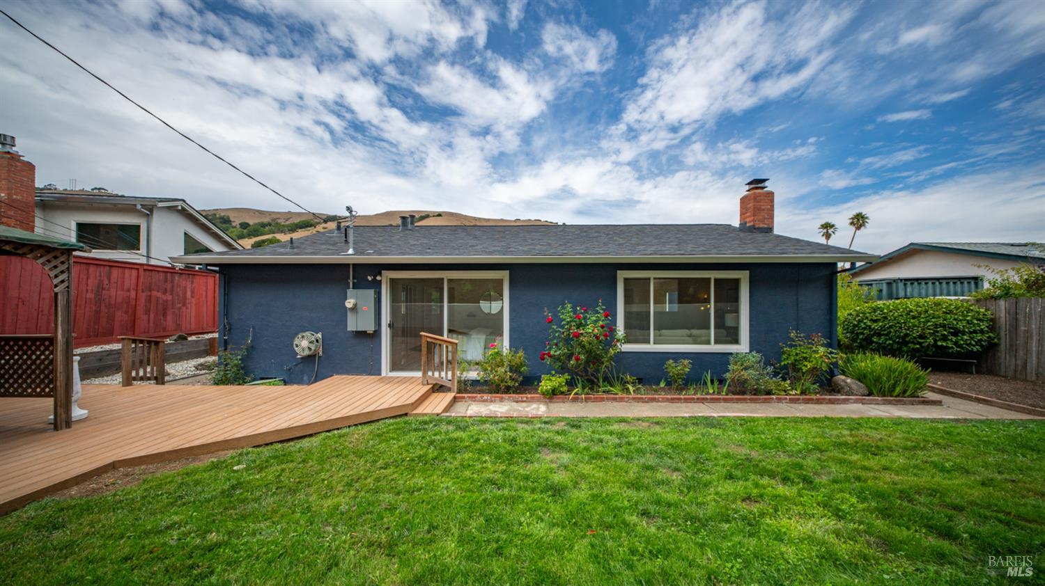 Blue single-story house with a wooden deck opening onto a green lawn and garden.