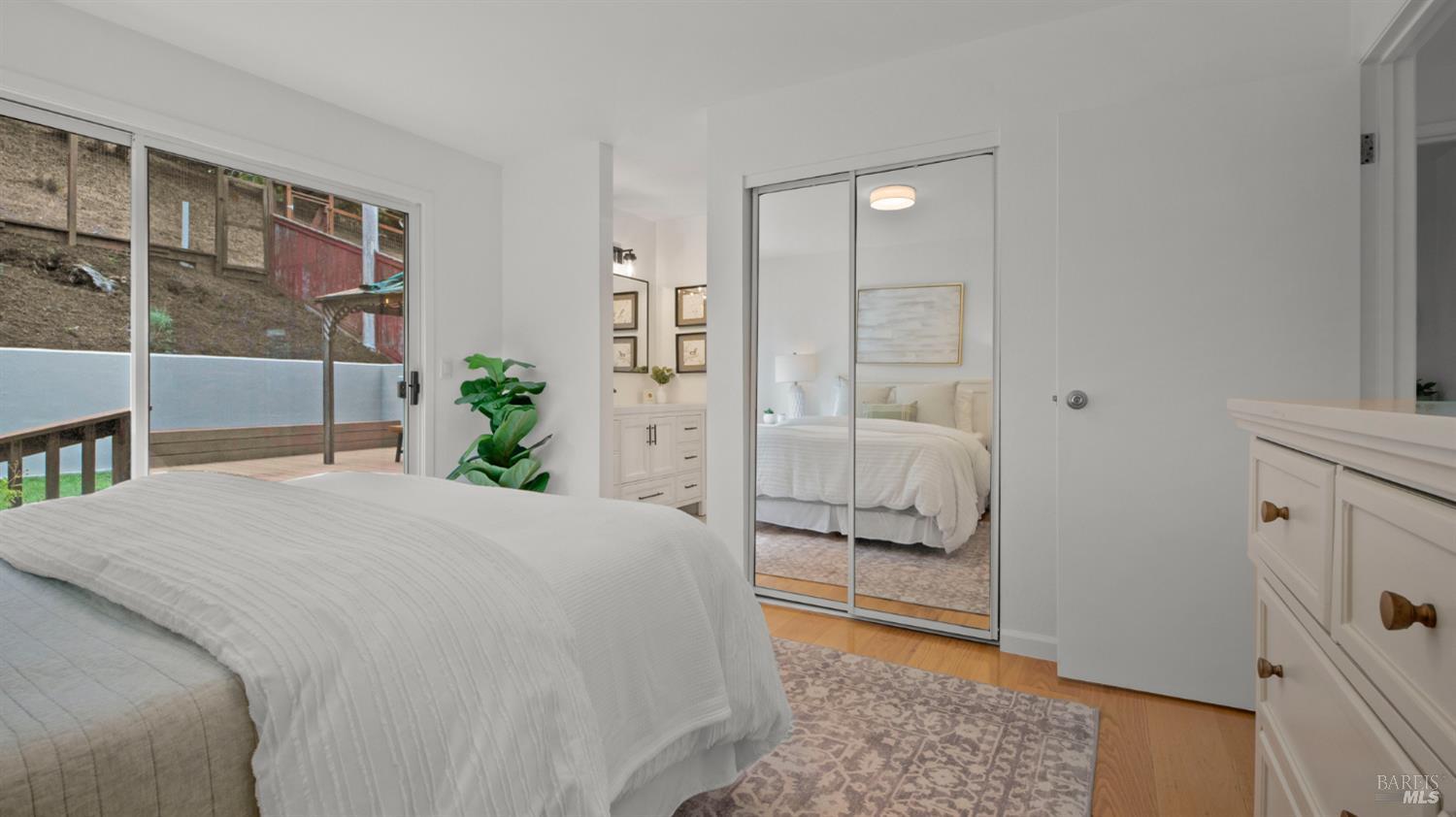Bedroom with a white bed, mirrored closet doors, and sliding glass doors opening onto a deck.