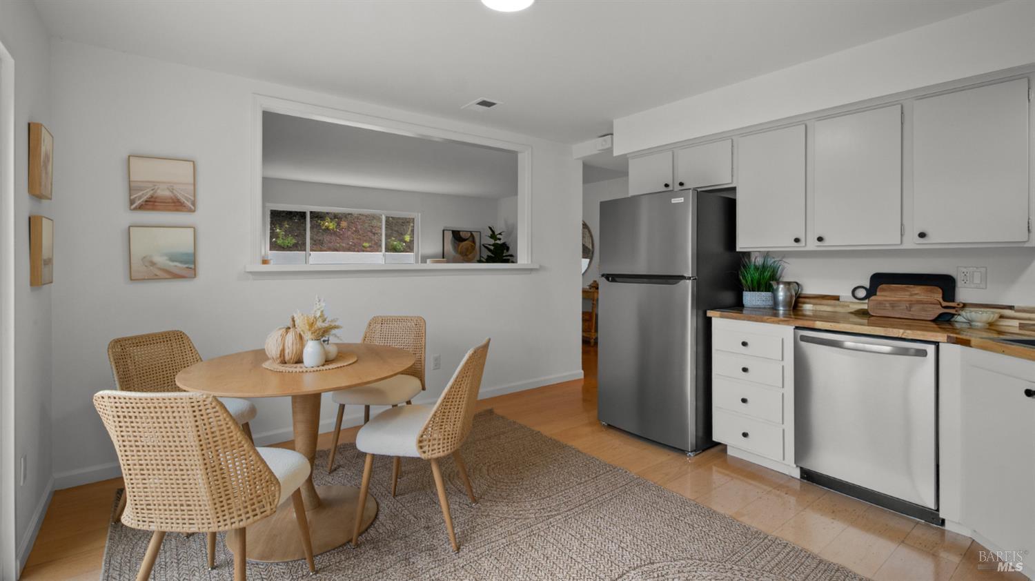 Dining area beside a white kitchen with stainless steel appliances and a wide interior pass-through.