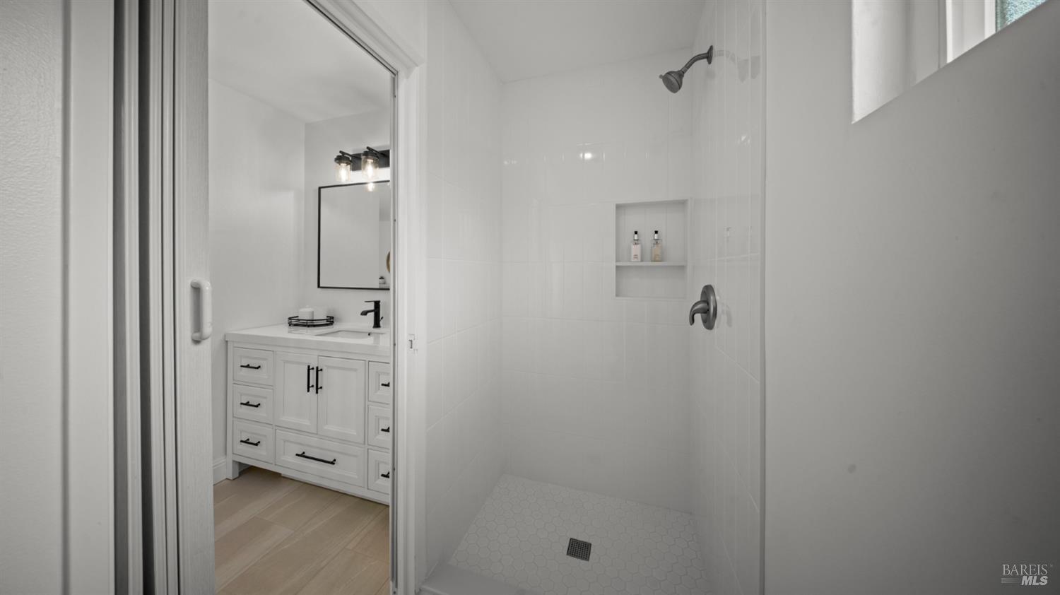 Bathroom with a white tiled walk-in shower and recessed niche beside a white vanity.