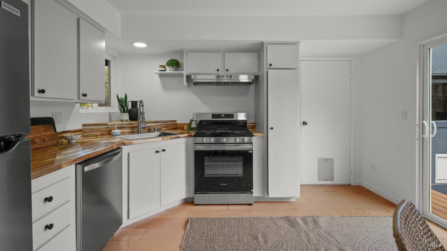 Kitchen with white cabinets, butcher-block counters, stainless steel appliances, and a gas range.