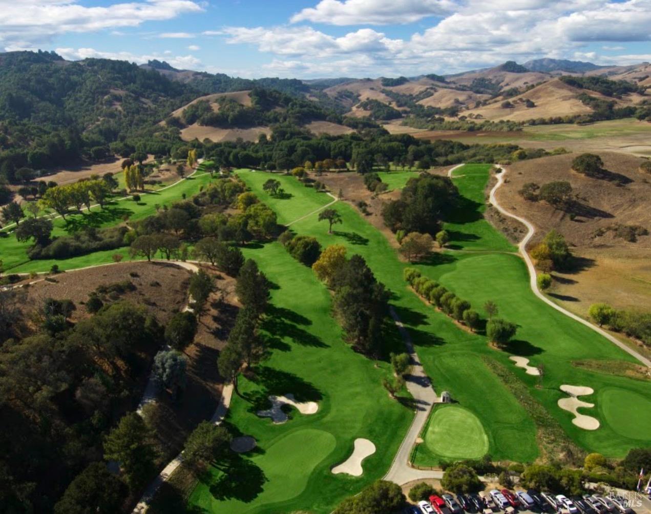 Aerial view of a golf course with green fairways and sand bunkers among rolling hills.