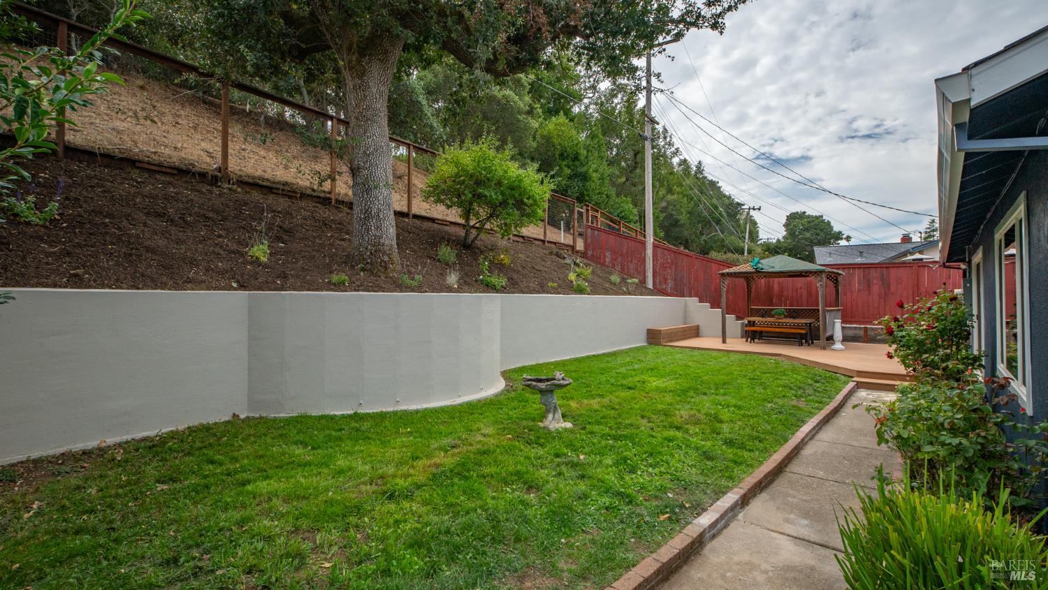 Backyard with a green lawn, curved retaining wall, and gazebo on a raised deck.